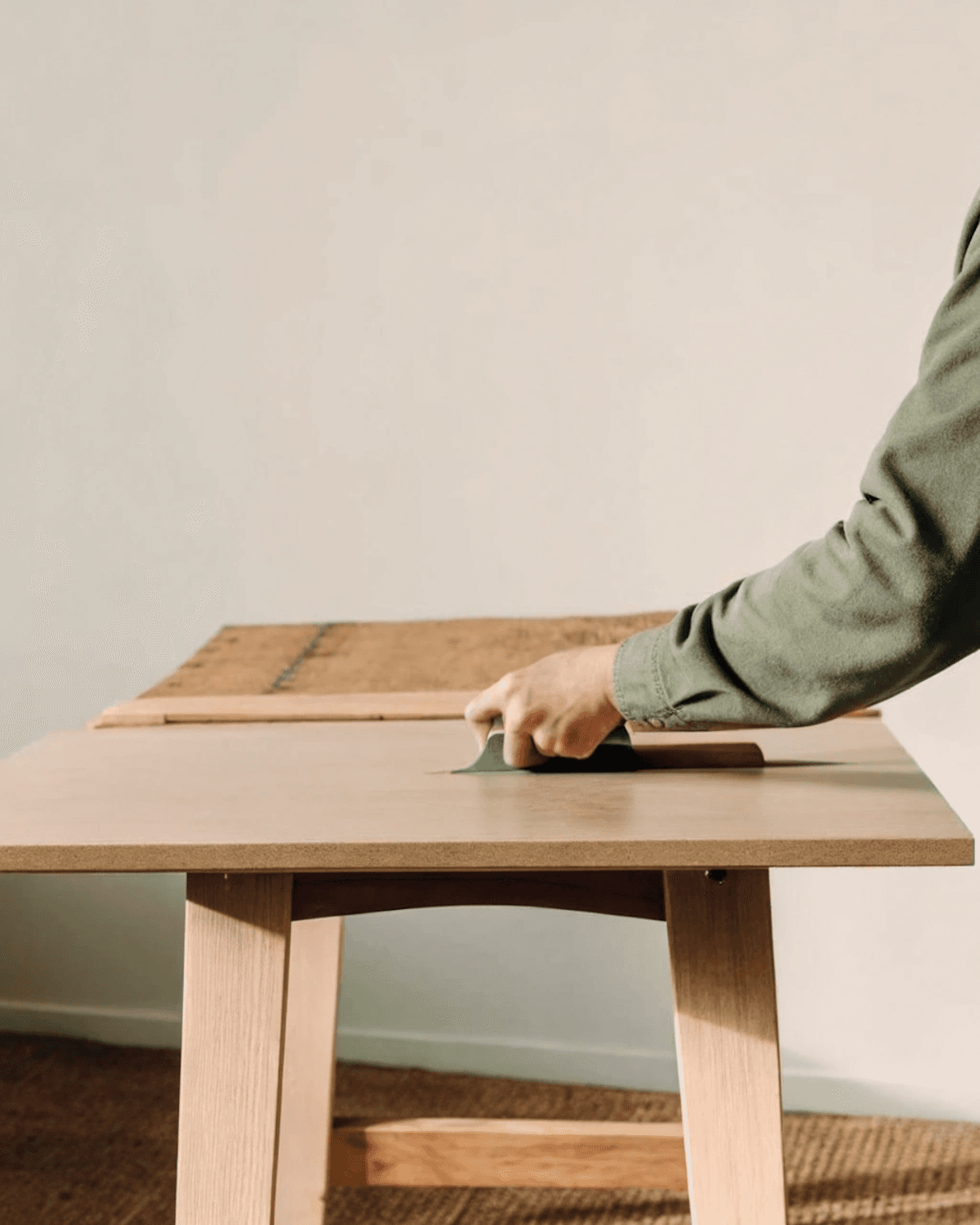 A maker sanding a light oak tabletop by hand in the Copenhagen workshop