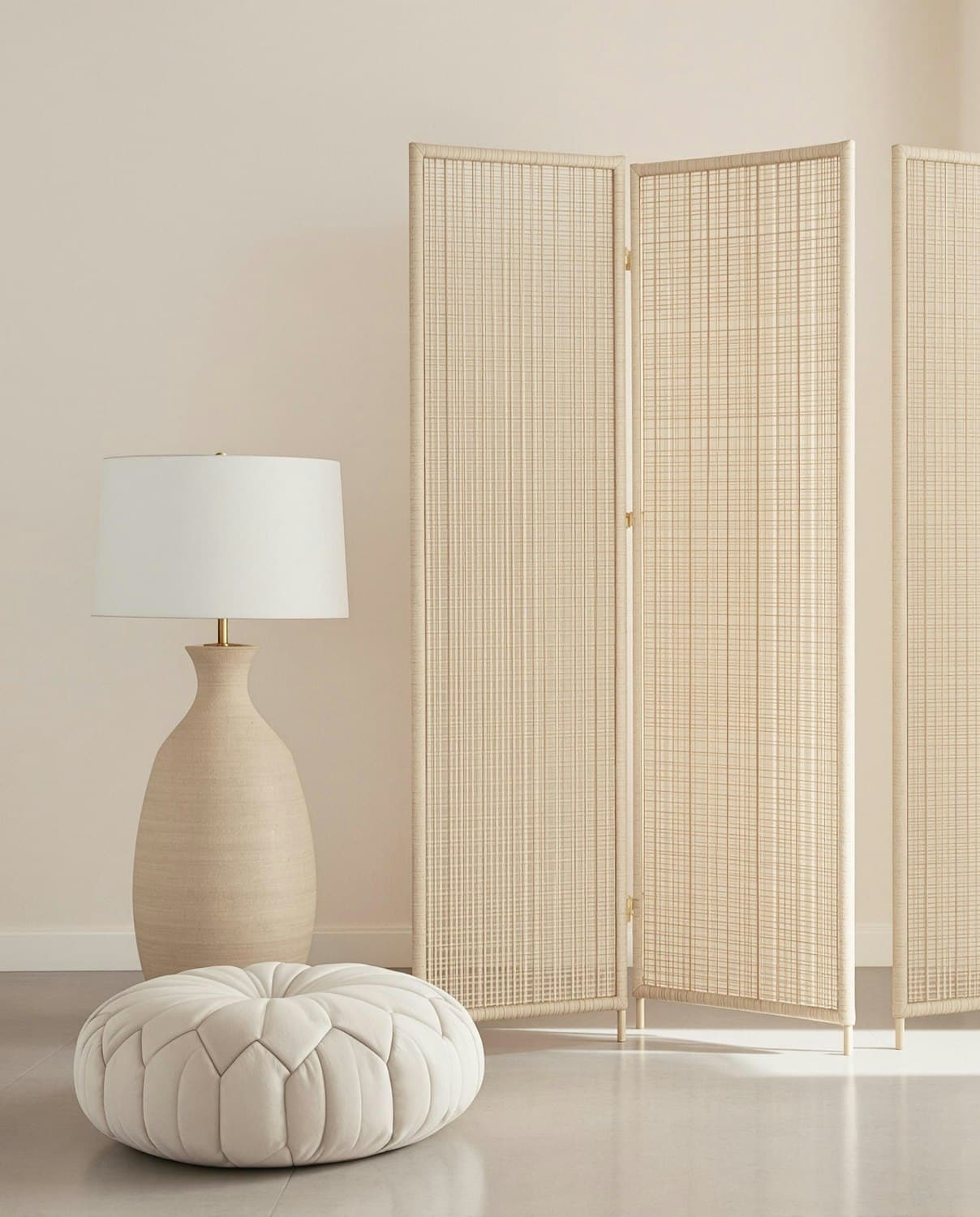Warm neutral interior with a woven shade lamp, cream ottoman and rattan screen